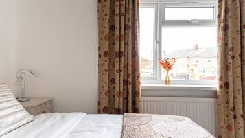 A bedroom with a bed, a nightstand, a lamp, and a window with curtains.