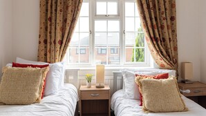 Une chambre avec deux lits, une table de chevet avec une lampe et une fenêtre avec des rideaux.