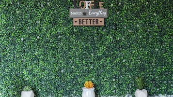 Un mur avec un décor de feuilles vertes et une pancarte sur laquelle on peut lire : « LE CAFÉ, ÇA AMÉLIORE TOUT ».