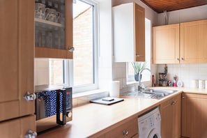 Een keuken met houten kastjes, een inbouwvaatwasser en een raam met uitzicht.