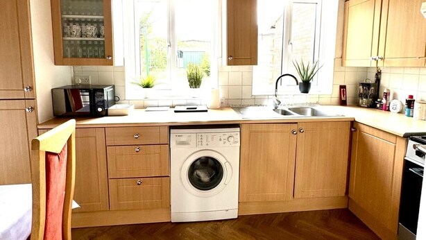 Une cuisine compacte avec des meubles en bois, un lave-linge et une fenêtre qui laisse entrer la lumière naturelle.