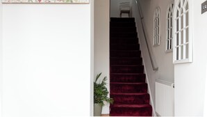 Un escalier recouvert d’une moquette rouge mène à un palier où est affiché un panneau d’accueil orné d’oiseaux et de fleurs.