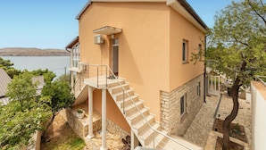 A two-story building with a stone foundation and a beige exterior. It features a set of stairs leading to a balcony with a metal railing.