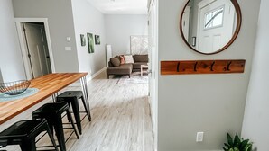Een moderne woonkamer met een houten eettafel, zwarte barstoelen, een grijze bank en een ronde spiegel aan de muur.