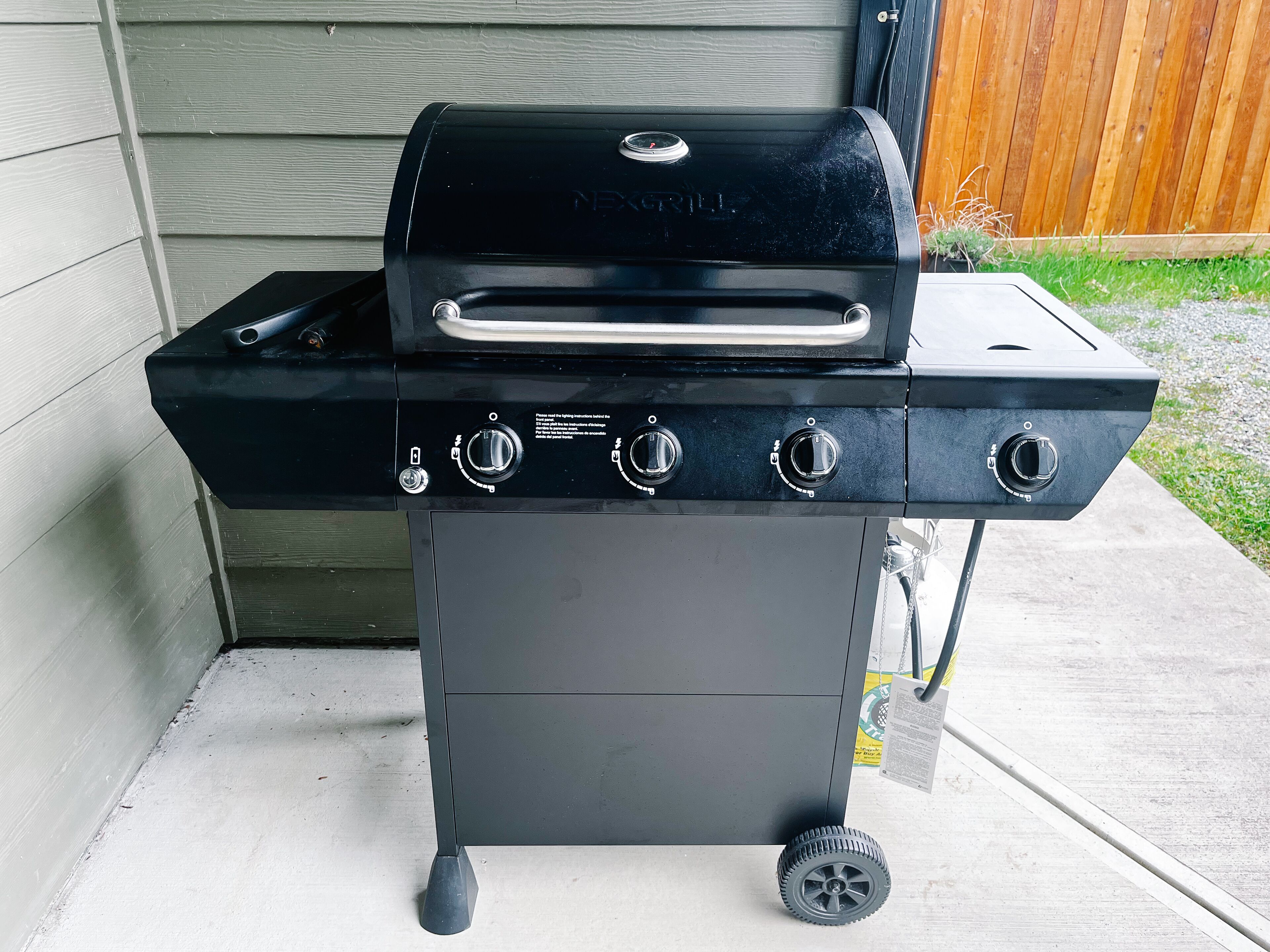 A black outdoor grill with four control knobs and a side burner, mounted on a wheeled cart.