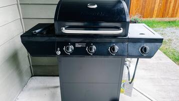 A black outdoor grill with four control knobs and a side burner, mounted on a wheeled cart.