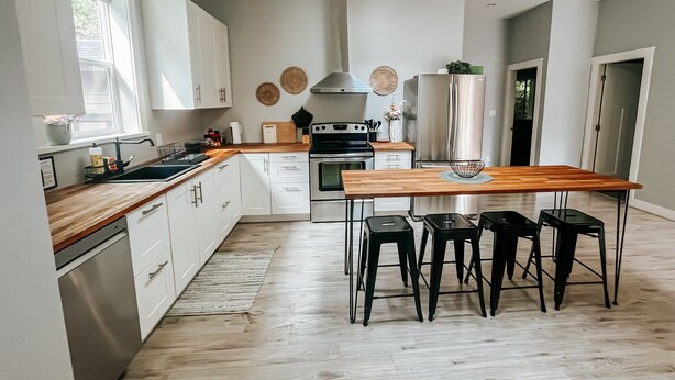 Een moderne keuken met witte kasten, een houten aanrecht, een roestvrijstalen koelkast en een eethoek met vier krukken.