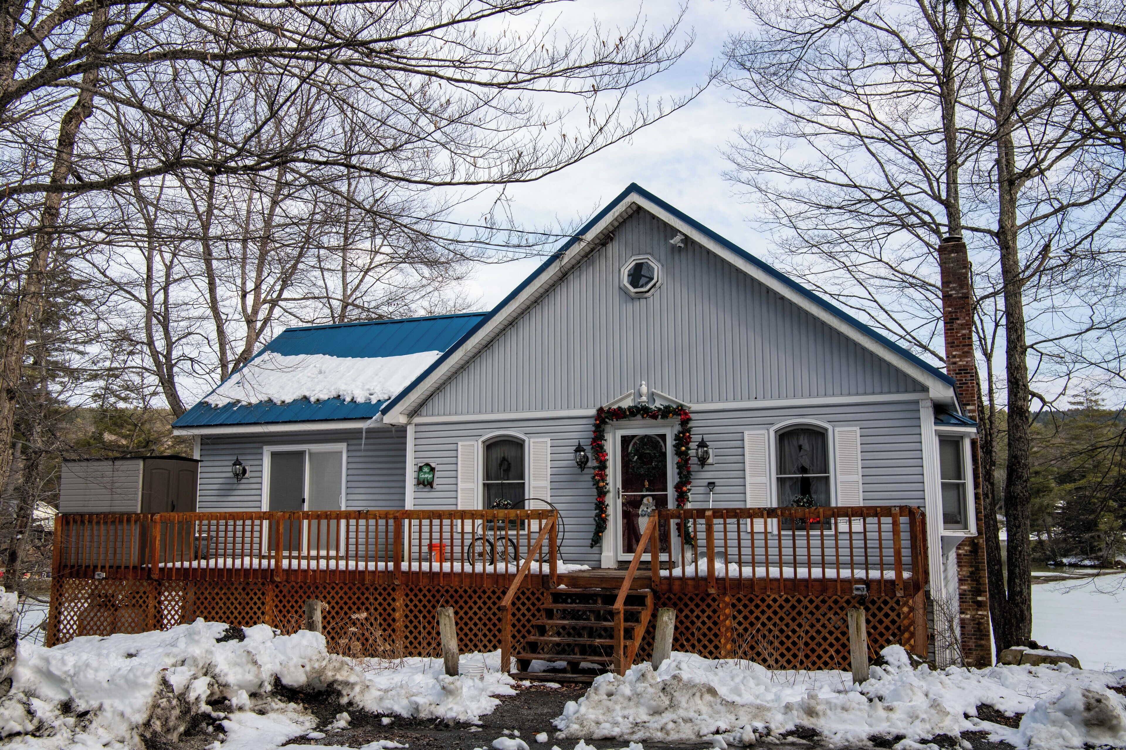 A two-story house with a blue roof, a front porch with a wooden railing, and a front door decorated with a wreath.