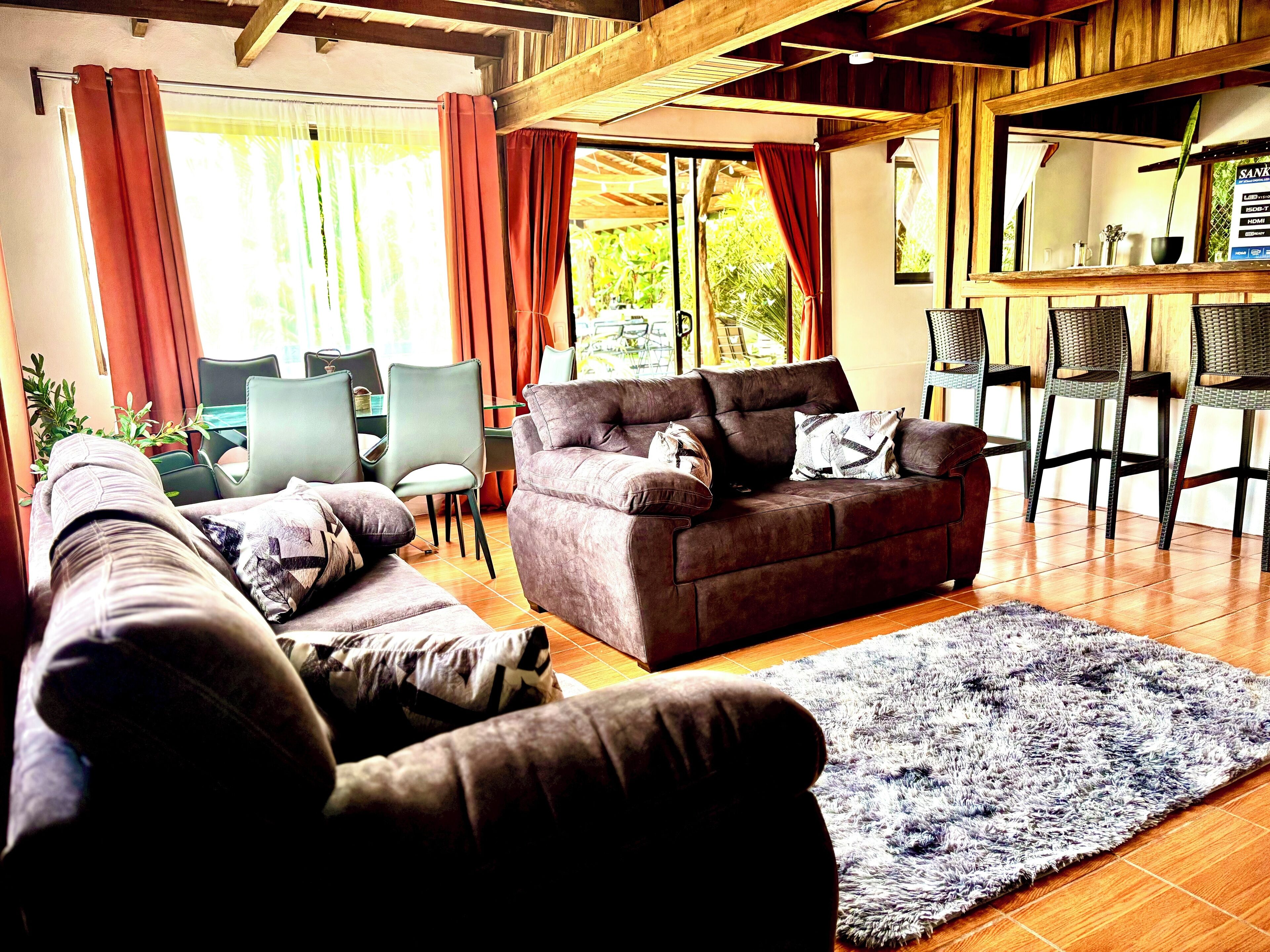 Una sala de estar con sofá, sillas, alfombra y un comedor con mesa y sillas.