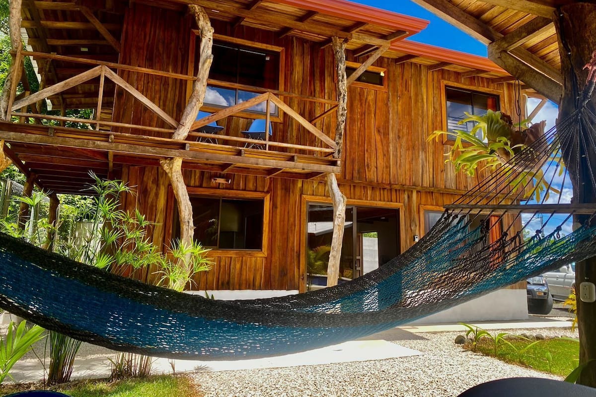 A wooden cabin with a hammock, surrounded by greenery.