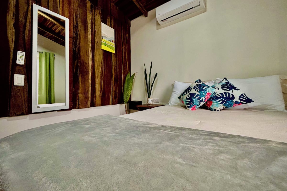 A bedroom with a wooden wall, a bed with white bedding, a green curtain, and a potted plant.