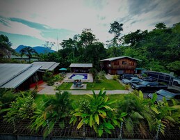 Un resort con piscina, mobiliario exterior y zona de estacionamiento rodeado de exuberante vegetación y plantas tropicales.