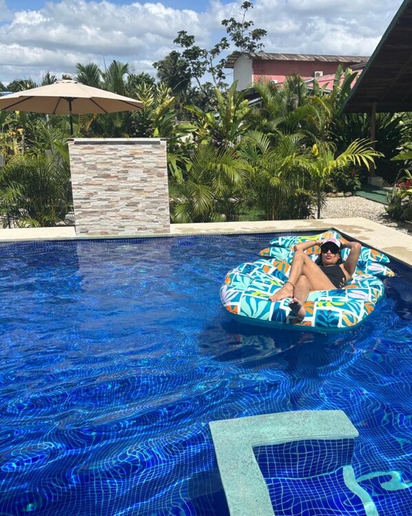 A swimming pool with a person lying on an inflatable float. - Cabañas Litos (La Fortuna)