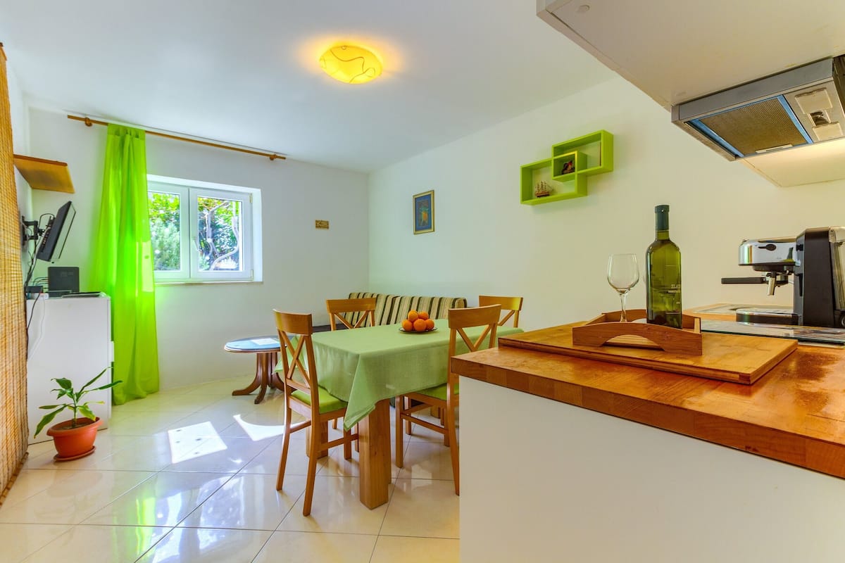 Comedor con mesa lista para cuatro, barra de cocina y ventana con cortinas.