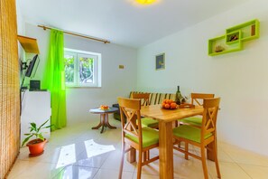 A dining area with a wooden table and chairs, a potted plant, and a window with curtains. - Apartments Filipovic with garden (Split)