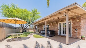 A patio area with a table and chairs, a covered seating area, and a brick building with a glass door. - Charming 4-bedroom house, family and pet friendly, in desirable east Tucson! (Tucson)