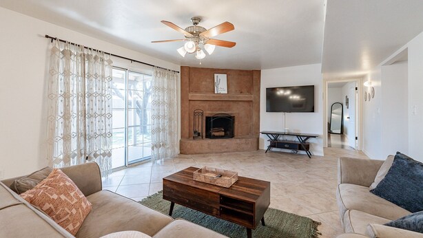 A living room with a fireplace, a ceiling fan, and a television. - Charming 4-bedroom house, family and pet friendly, in desirable east Tucson! (Tucson)