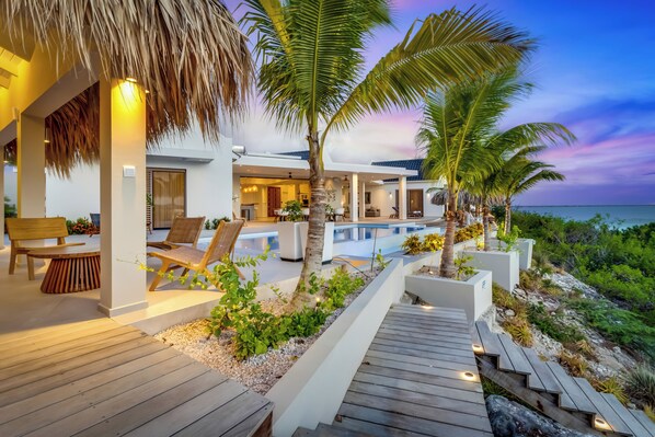 A modern resort with a wooden deck, lounge chairs, and a pool area. - Luxurious oceanfront villa with private cinema and private pool! (Kralendijk)