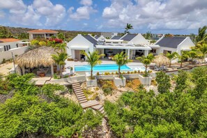 A modern resort with a swimming pool, thatched-roof structures, and lush greenery. - Luxurious oceanfront villa with private cinema and private pool! (Kralendijk)
