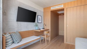 Une pièce de taille modeste, comprenant un banc en bois, un bureau avec une chaise, un téléviseur fixé au mur et une armoire.