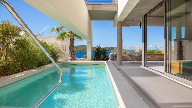 Un espace piscine avec une eau cristalline, entouré de plantes et offrant une vue sur la mer.