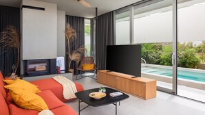 Un salon moderne avec un canapé, une table basse, un téléviseur et une vue sur une piscine.
