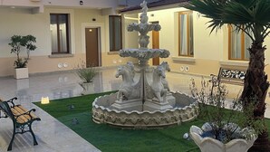 A courtyard with a central fountain, a palm tree, and a bench. - hotel du parc canal (Saint-Denis)