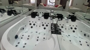 A large, white, freestanding bathtub with multiple jets, positioned in a spacious bathroom with a large mirror reflecting the room. - hotel du parc canal (Saint-Denis)