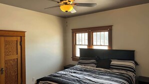 A bedroom with a bed, a ceiling fan, a window, and a wooden door.