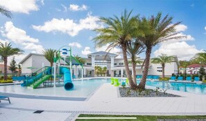 A swimming pool area with a water slide, palm trees, and a building with a white facade.