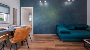A modern dining area with a wooden floor, a table set with pink plates and glasses, and a teal sofa. - Beautiful apartment in Galizana (Galizana)