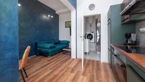 A modern kitchen with a coffee maker, a washing machine, and a dining area with a blue sofa and wooden chair. - Beautiful apartment in Galizana (Galizana)