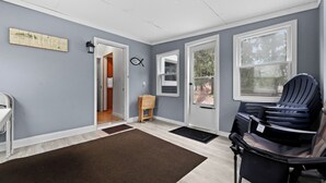Una habitación con una pared azul claro, suelo de madera, una silla marrón y negra, una mesita pequeña y una puerta que da a otra habitación.