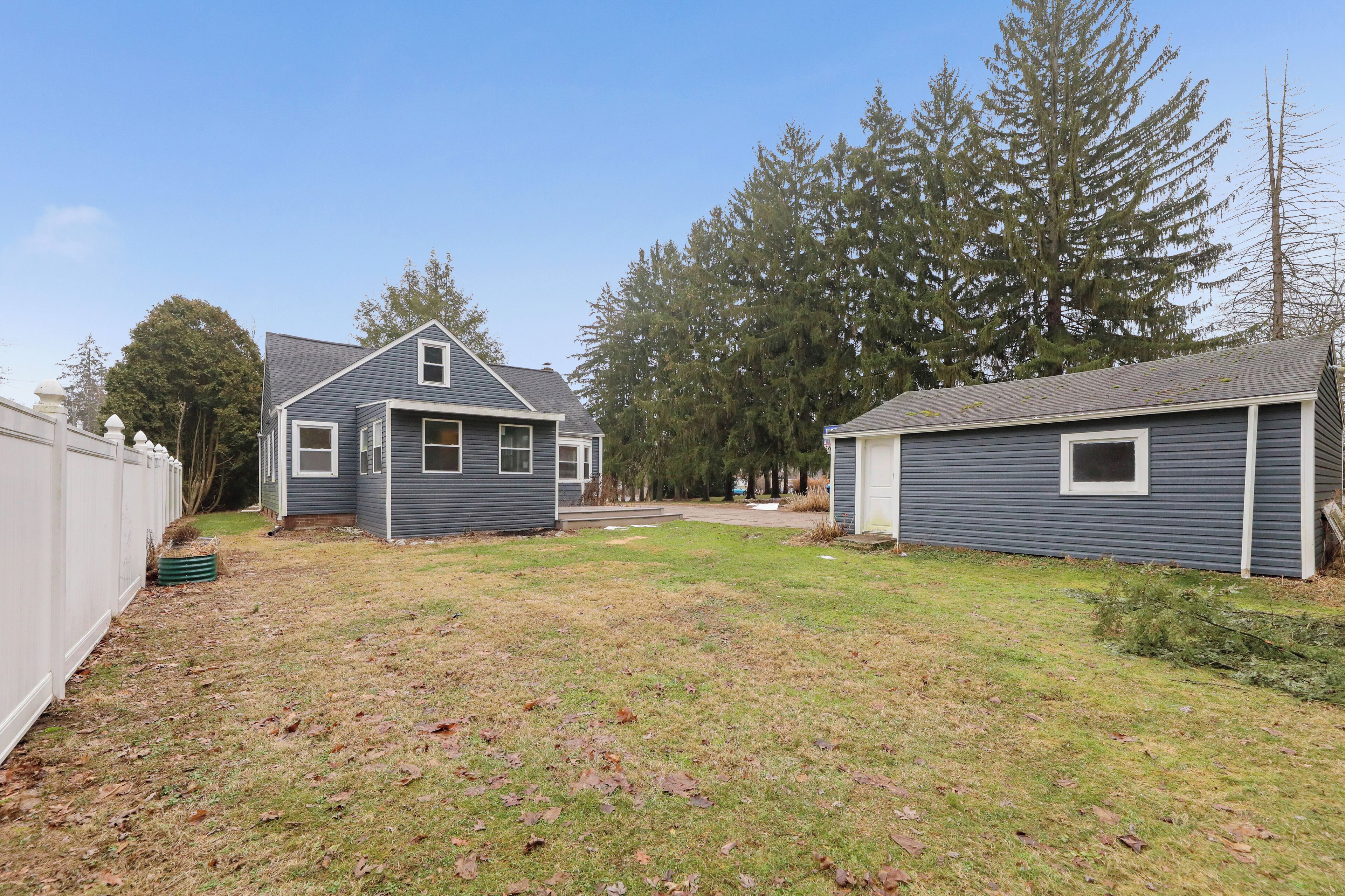 A residential property with two houses, a grassy yard, and tall trees.