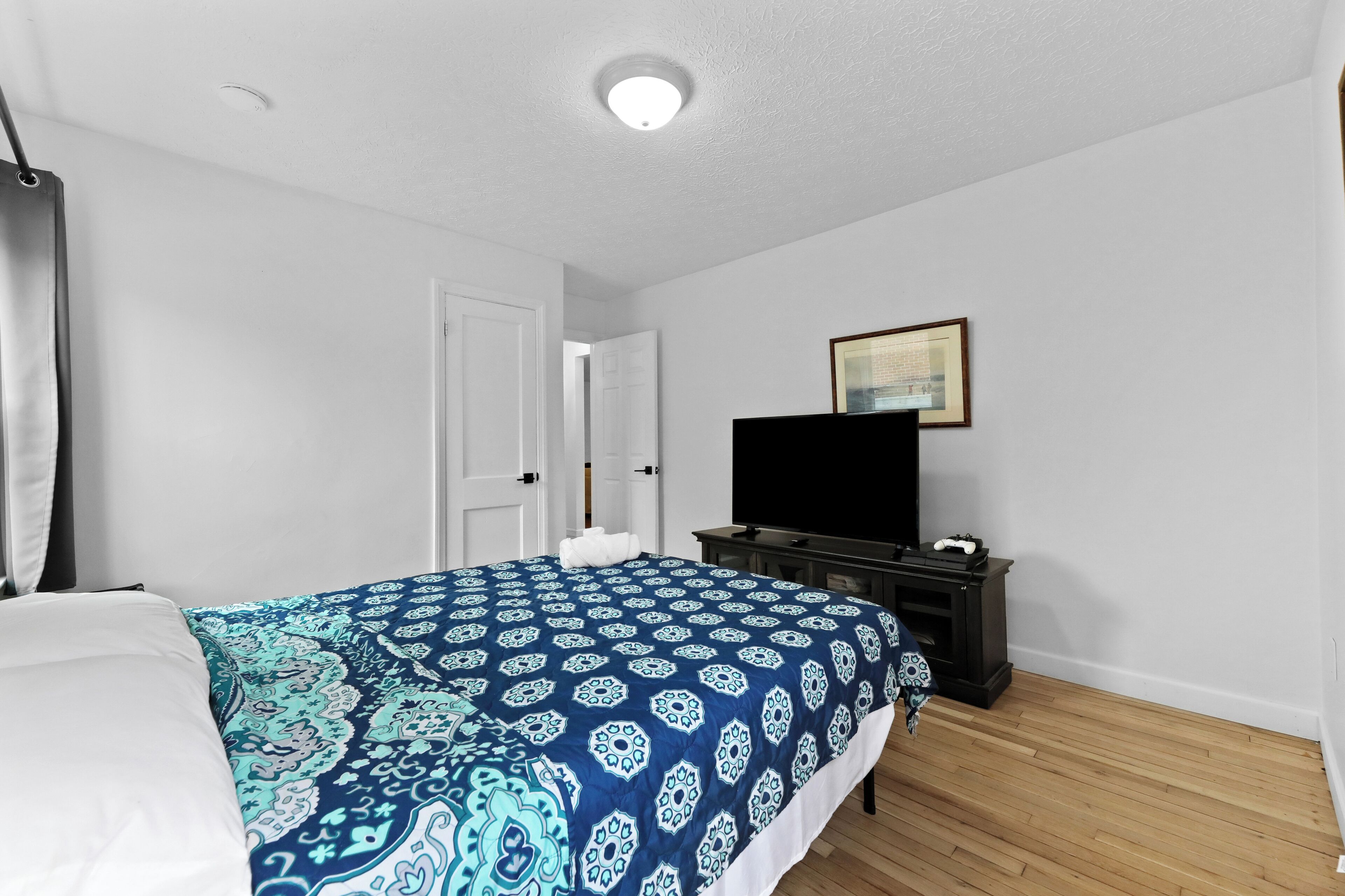 Ein Schlafzimmer mit Bett, Kommode, Fernseher und Tür.