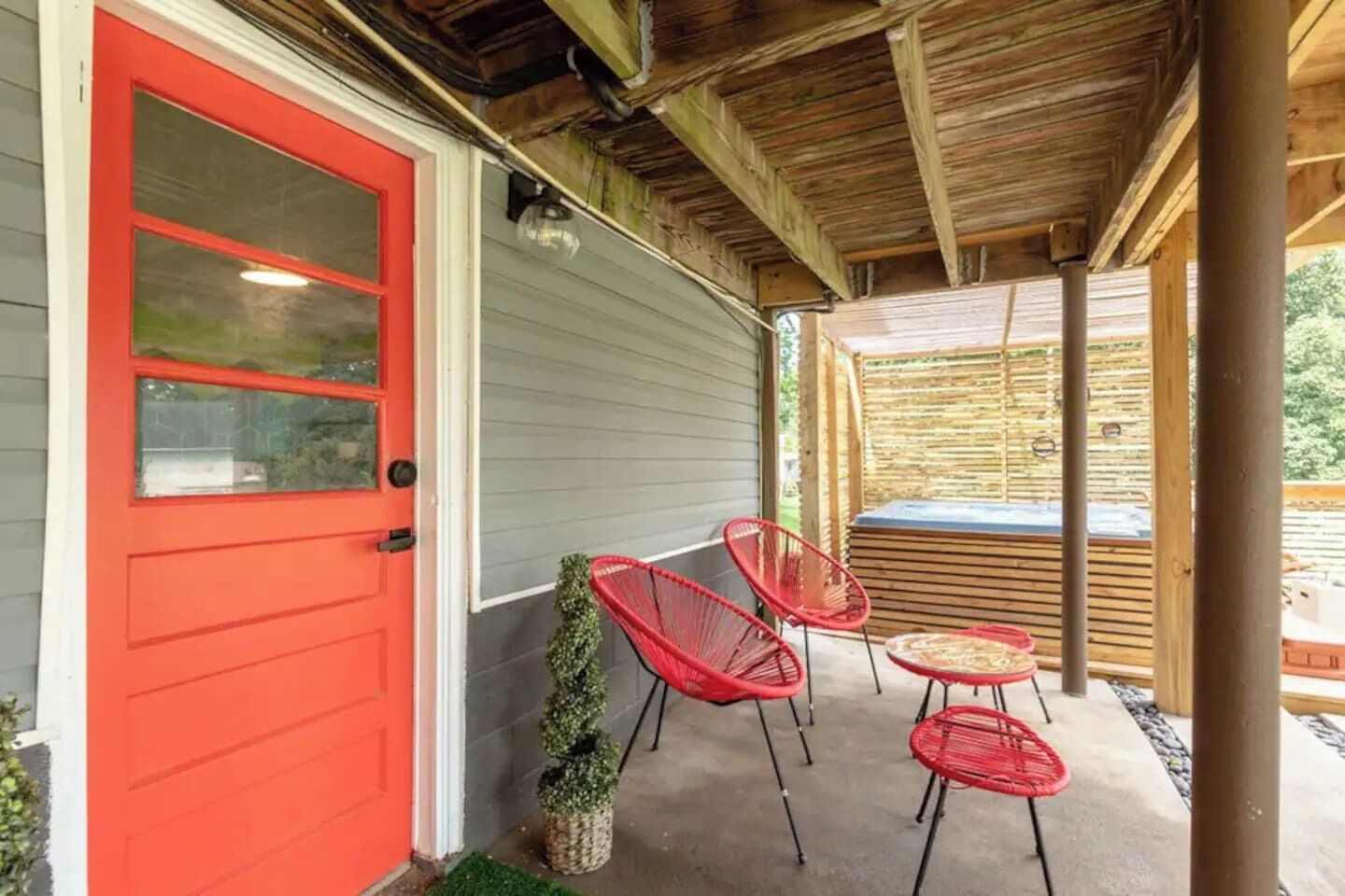 A covered porch with a red door, two red chairs, and a small table.