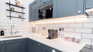 Una cocina moderna con armarios azul oscuro, encimera blanca, microondas integrado y cafetera.