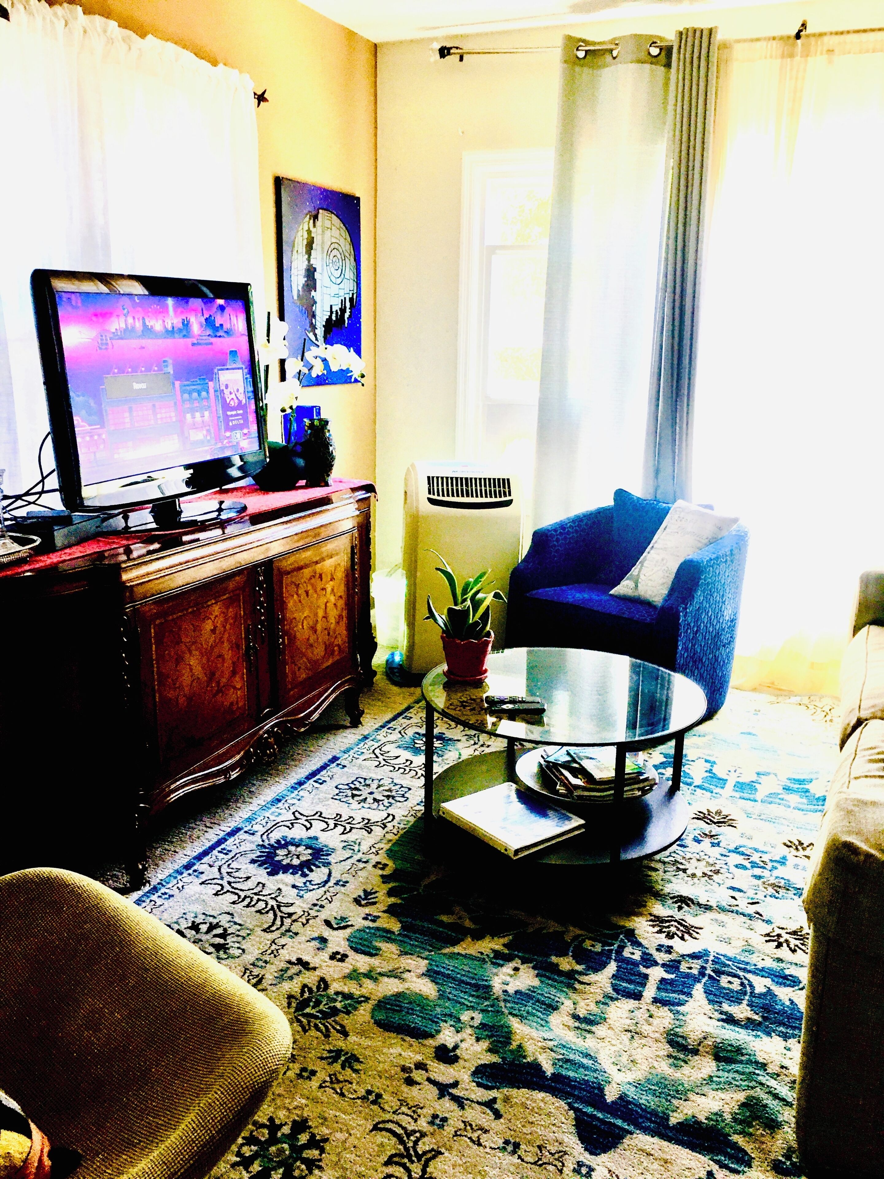 Ein Wohnzimmer mit Fernseher, blauem Sessel, Couchtisch und einem gemusterten Teppich.