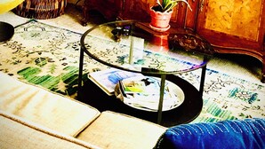 Ein Wohnzimmer mit Fernseher, Zimmerpflanze, Korb aus Weidengeflecht und Glastisch.