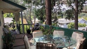 Eine überdachte Terrasse mit einem Glastisch und Stühlen, umgeben von Topfpflanzen und Blick auf Häuser.