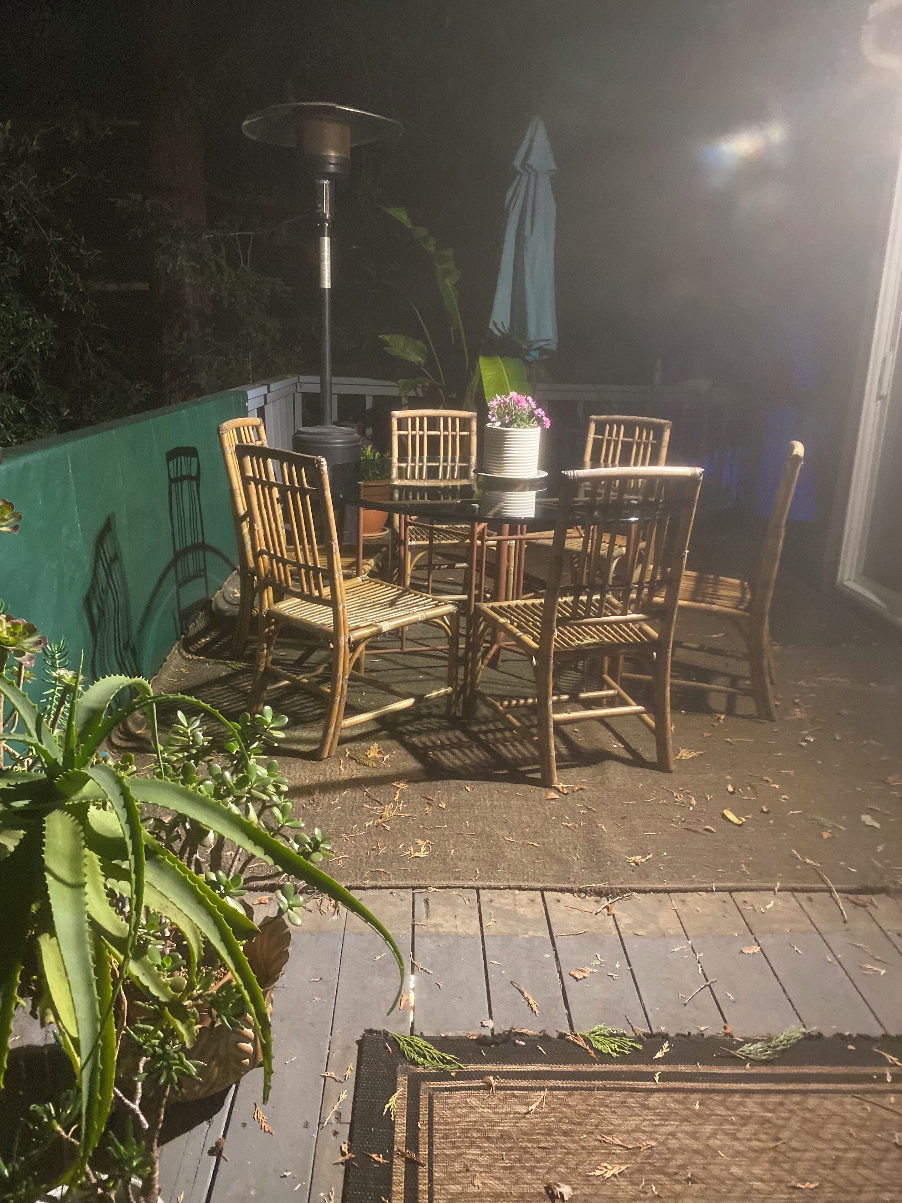 An outdoor patio with a round table and four chairs, surrounded by potted plants and a green wall.