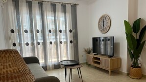 A living room with a sofa, a TV on a wooden stand, a small round table, and a large potted plant. - Geranium in Javea X bia (Javea)