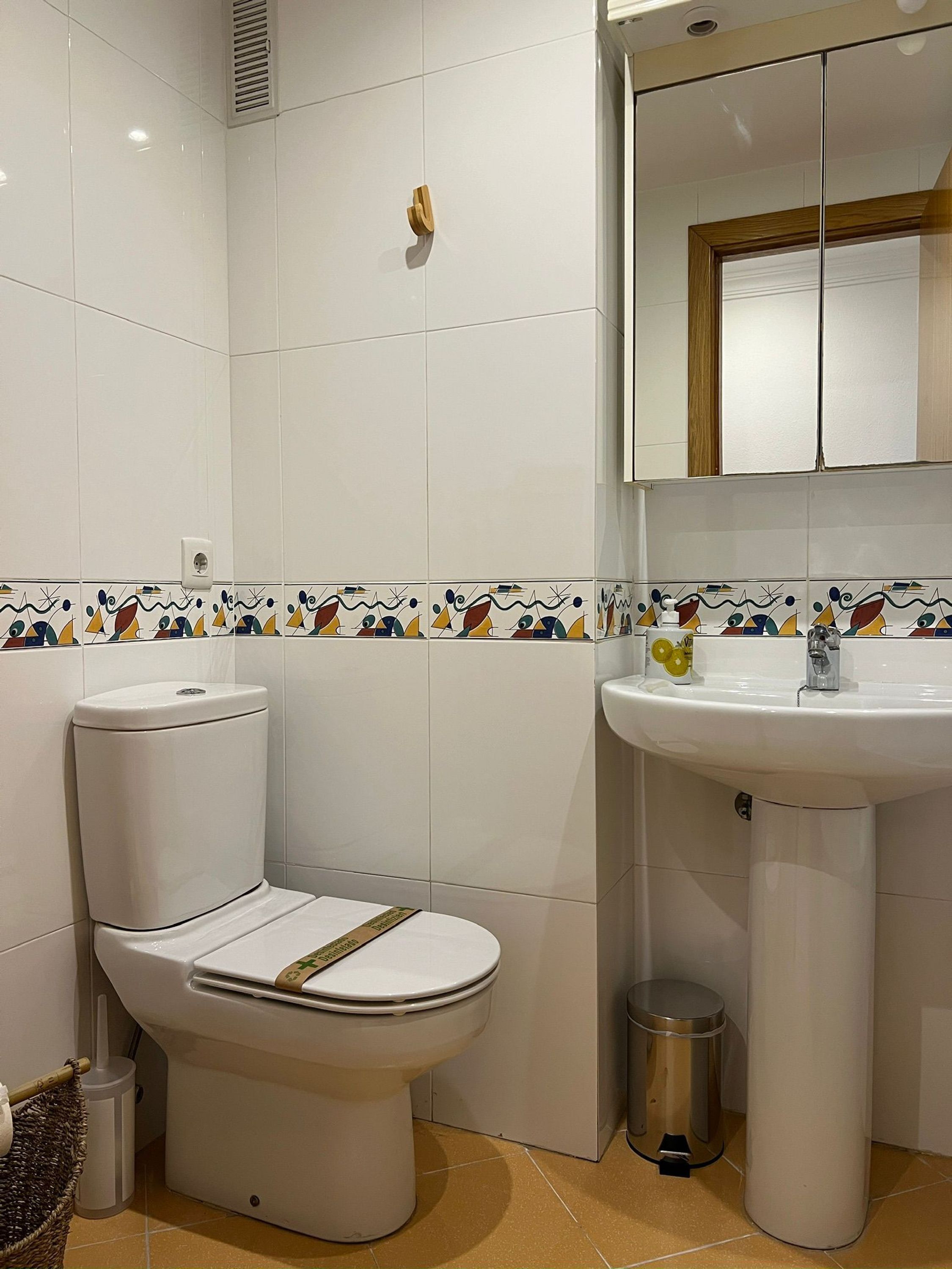 Un baño con inodoro, lavamanos y un cubo de basura.