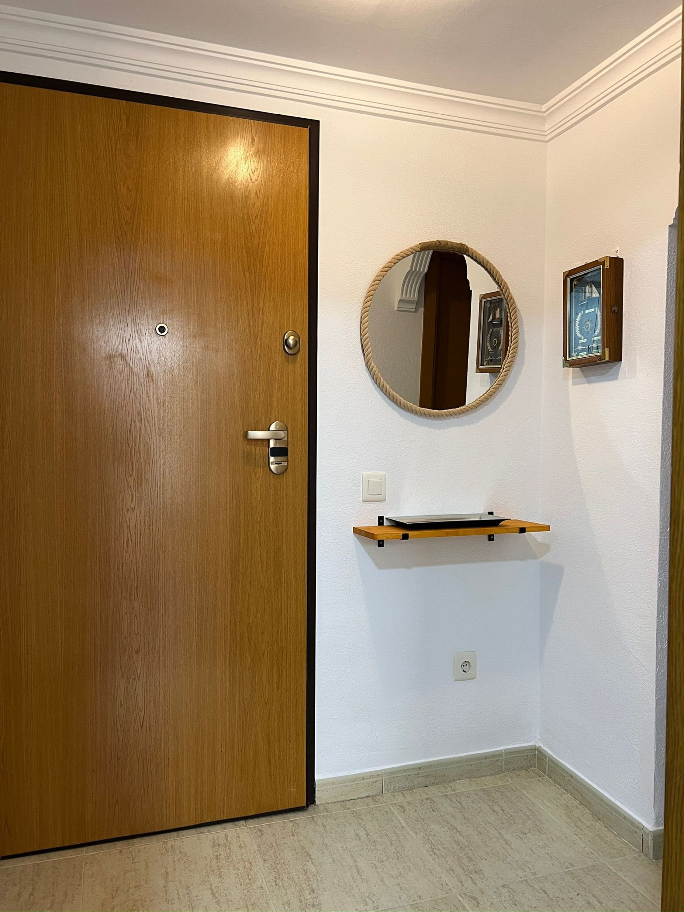 A room with a wooden door, a round mirror, a small shelf, and a wall socket.