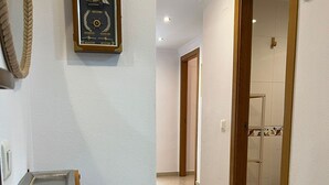 A hallway with a wall-mounted clock, a shelf, and a door leading to a bathroom. - Geranium in Javea X bia (Javea)