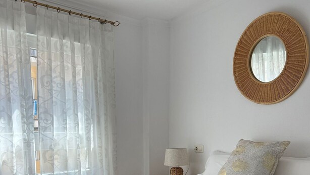 A neatly made bed with white linens and towels, a round woven mirror on the wall, a bedside lamp, and a window with sheer curtains. - Geranium in Javea X bia (Javea)