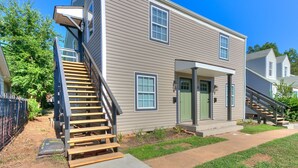 A two-story house with a wooden staircase leading to the front door, a small front porch, and a well-maintained lawn.