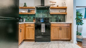 A modern kitchen with wooden cabinets, a black refrigerator, a stove, and a tiled backsplash.