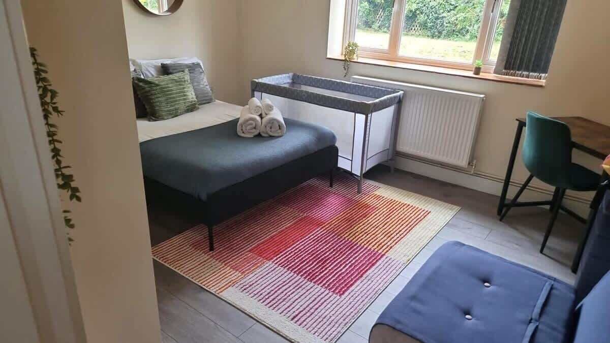 A compact room with a bed, a small desk, a chair, and a window with a view of greenery.