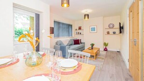 A modern living room with a dining area, a sofa, a TV, and a wooden door. - Spacious 2BR Flat @ Summertown | Sleeps 7 | 5 Star (Oxford)
